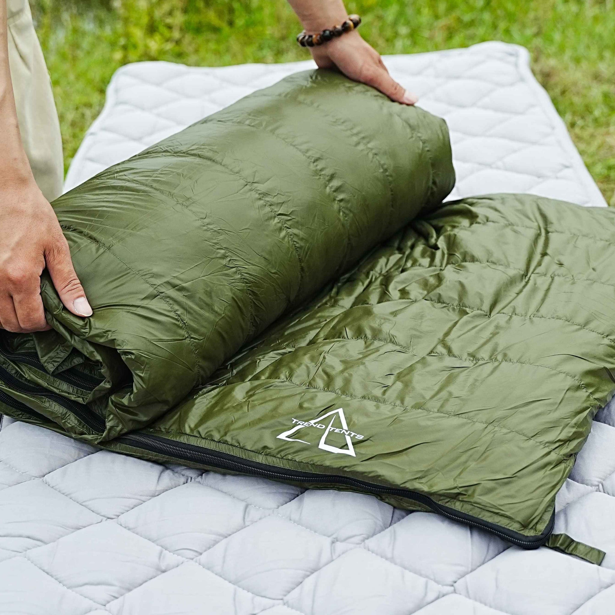 Green sleeping bag being unrolled on a white quilt outdoors