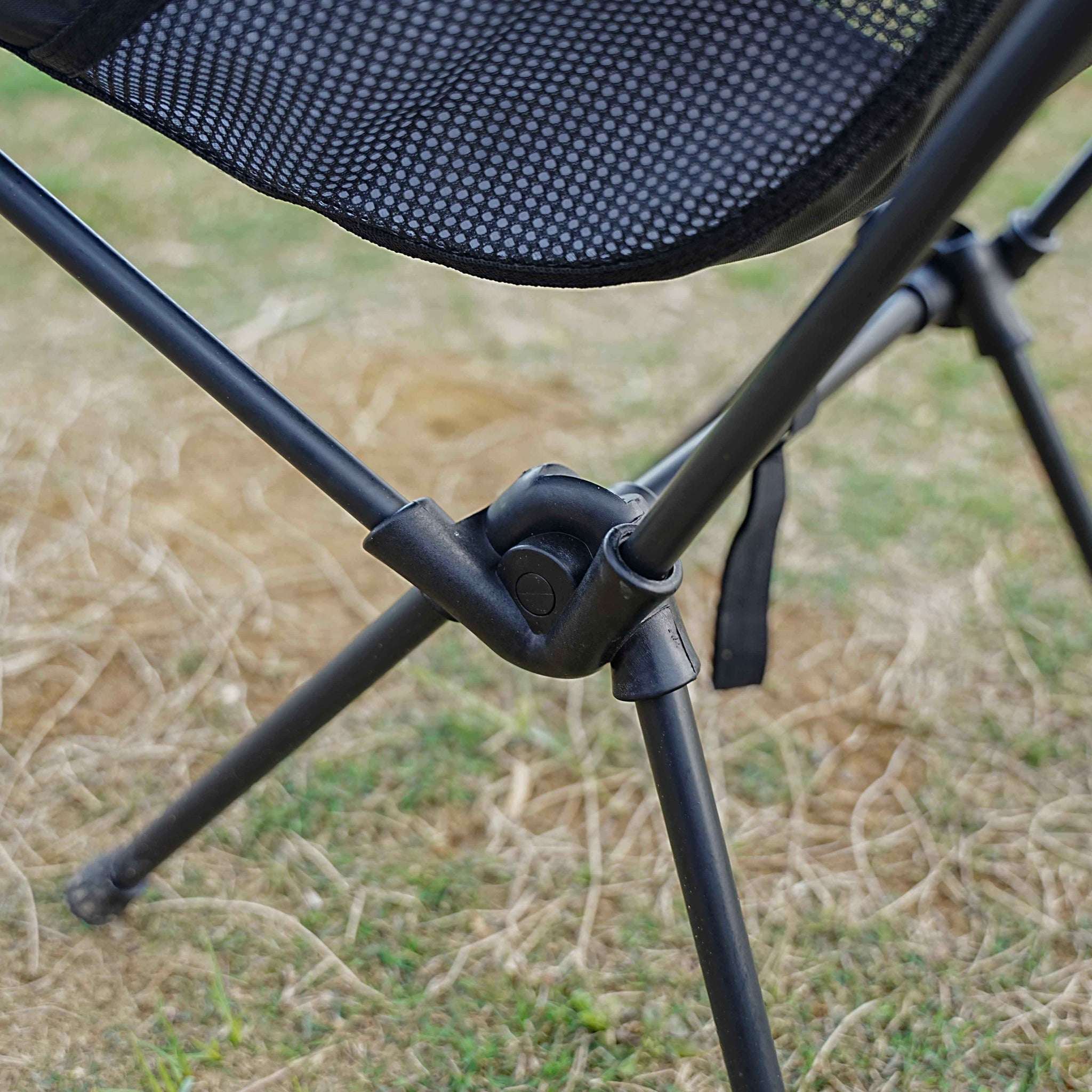 Close-up of a black camping chair with mesh backrest on grass