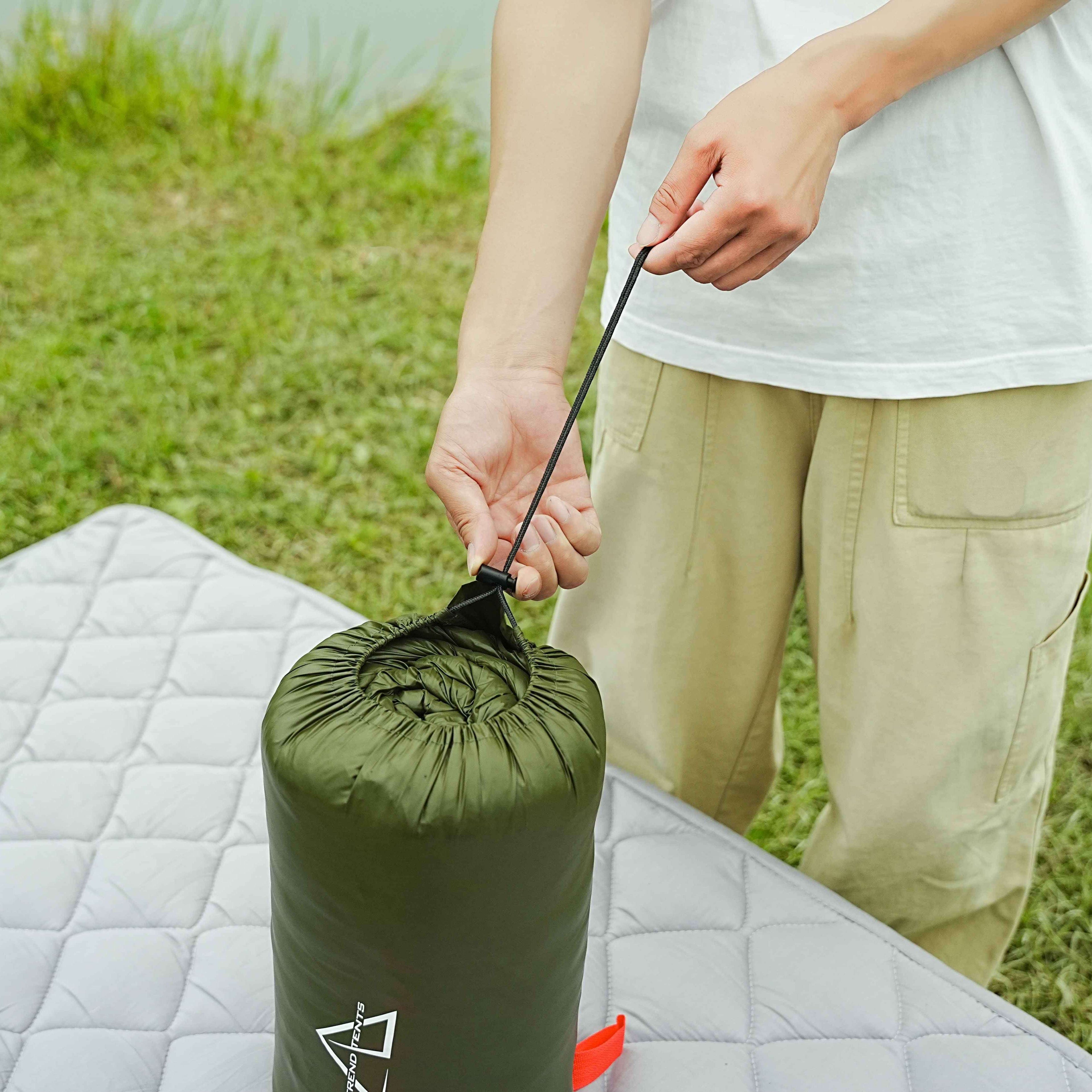 Person unpacking a green sleeping bag on a grassy outdoor setting